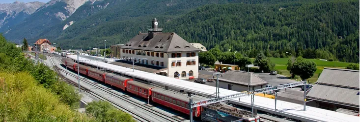 Red train at the platform in a station surrounded by mountains