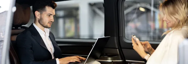 Two passengers are using a computer and a phone in a vehicle
