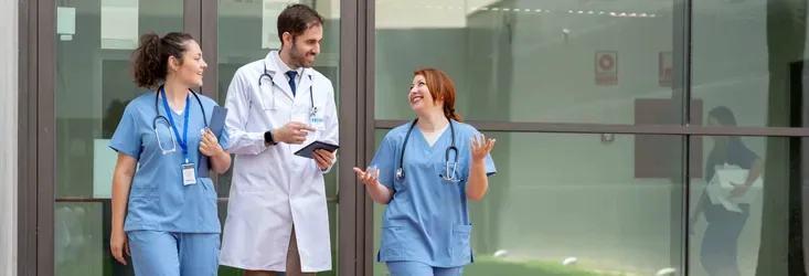 Three healthcare professionals in front of a glass building